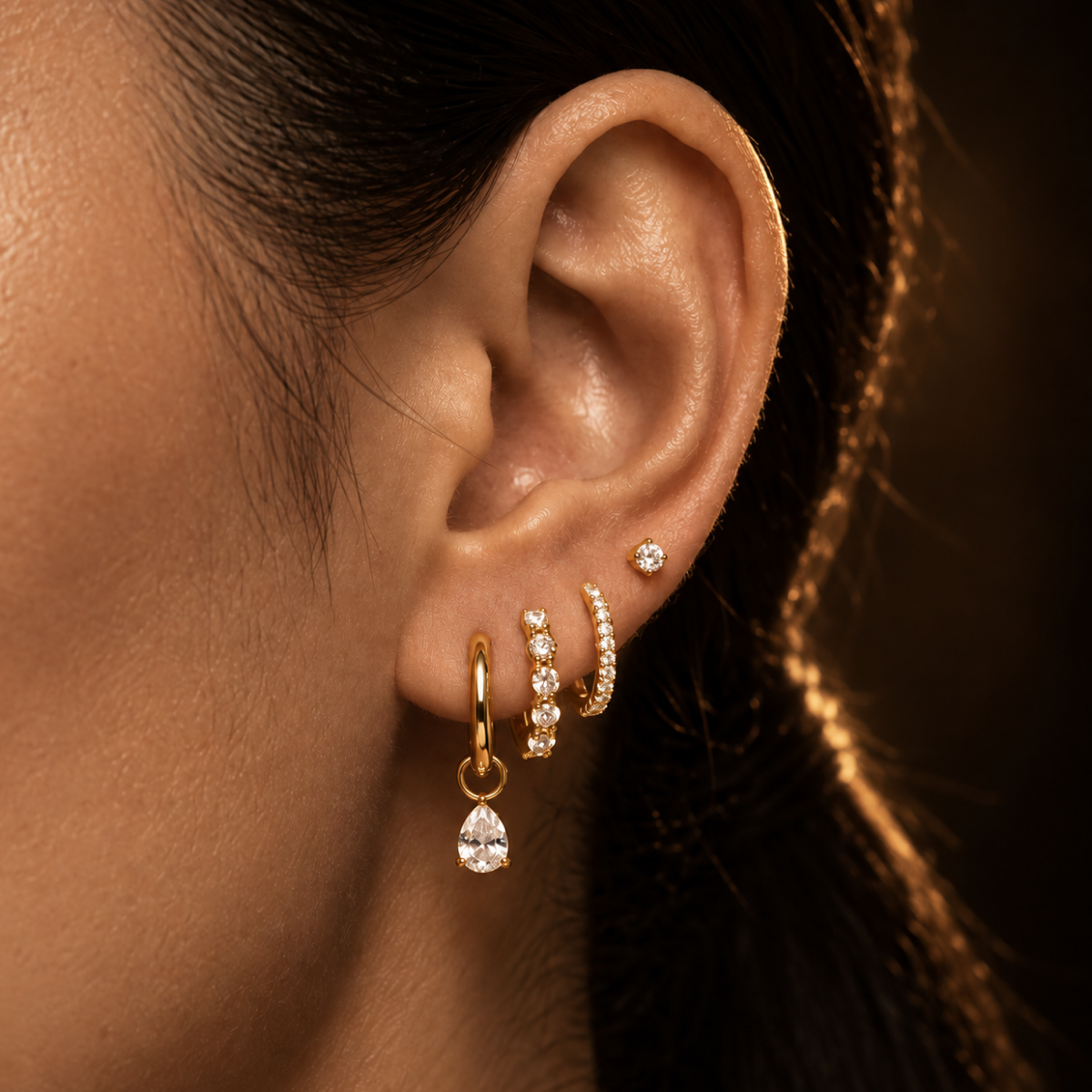 IMBER gold hoops with crystal details and a pear-shaped drop worn on ear